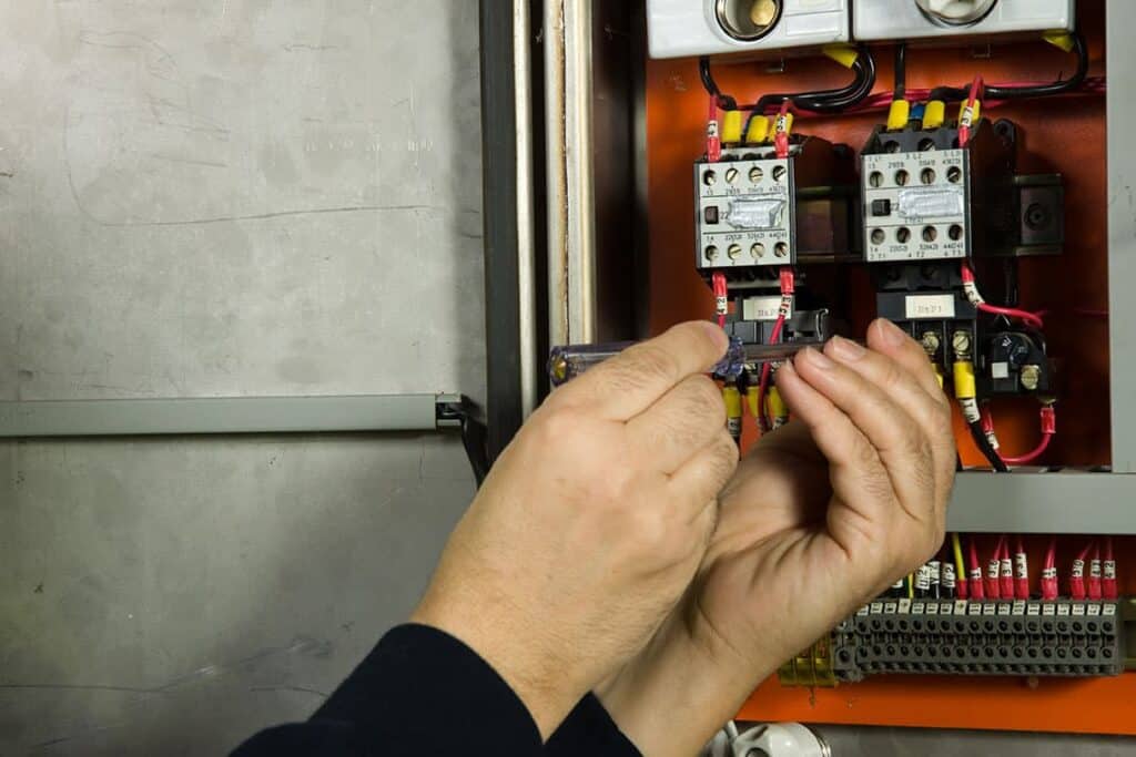 A person uses a screwdriver to adjust wiring inside an open electrical control panel.