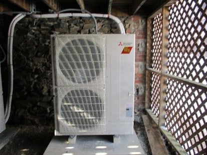 Outdoor condenser unit for Mitsubishi ductless mini split system installed under porch.