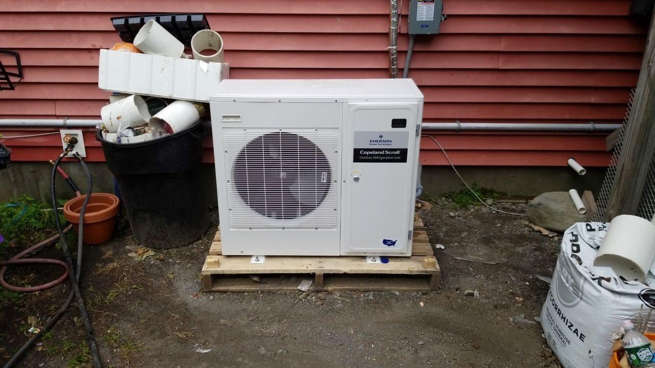 Outdoor condenser unit improperly installed behind a grocery store in MA. 