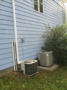 Side-by-side example of incorrectly installed 35-year-old HVAC system next to the new American Standard outdoor condenser unit on a concrete pad.