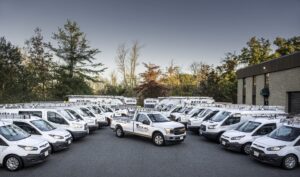 A fleet of white company vans and a pickup truck with "Keta Inc." logos are parked outside a commercial building, surrounded by trees.