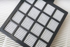 Close-up of a HEPA air filter with a black plastic frame, placed on top of another white pleated filter.