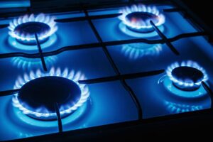 A close-up view of a gas stove with four burners lit, showing blue flames around each burner.