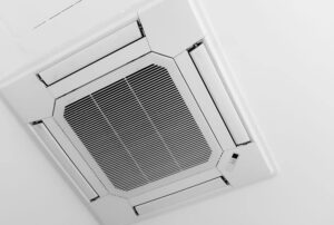 A ceiling-mounted air conditioning unit with vents and control panel installed on a white ceiling.