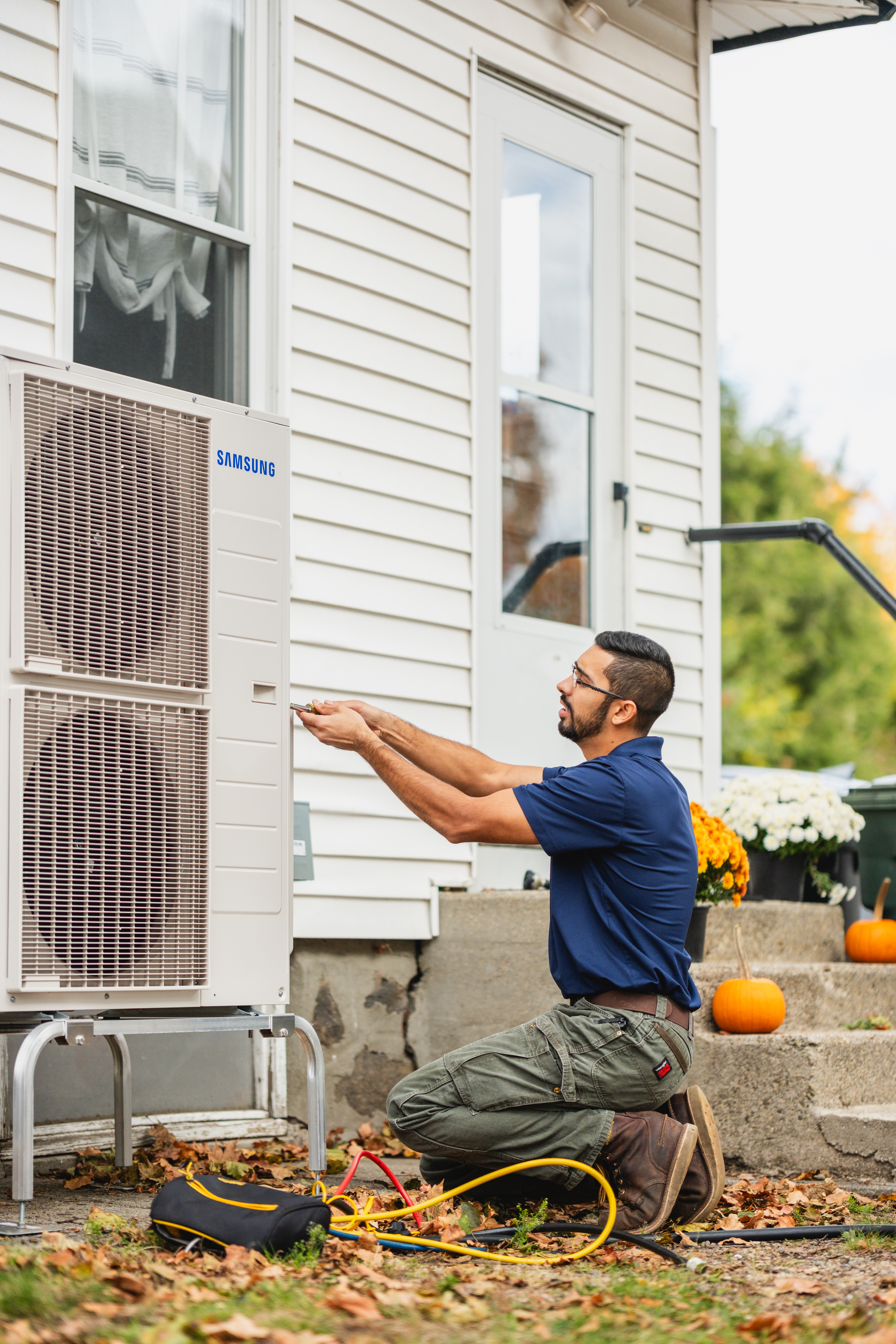 A man kneels down while performing maintenance on an outdoor AC unit.