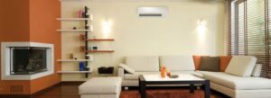 Modern living room with beige sectional sofa, coffee table, wall-mounted shelves, fireplace, air conditioner, and large window with blinds.