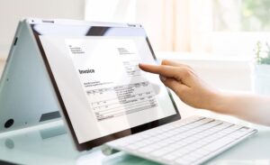 A person points to an electronic invoice displayed on a tablet screen next to a white keyboard.