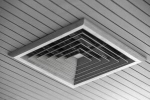 Square air vent with multiple concentric layers mounted on a slatted ceiling.