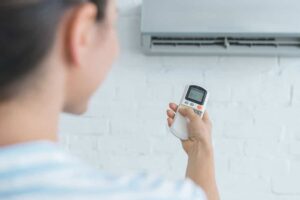 Person holding a remote control and pointing it at a wall-mounted air conditioner unit.