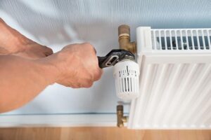 Person using a wrench to adjust or tighten a valve on a white radiator attached to a wall.