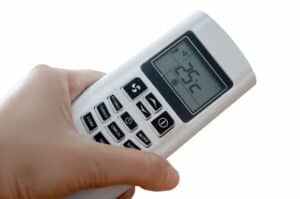 A hand holding a white remote control with a digital display showing a temperature setting of 25°C.