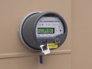 A digital electricity meter with a lock and tag attached is mounted on a beige wall, displaying a reading of 04166 kWh.