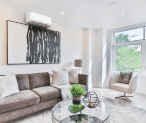 Modern living room with a brown sectional sofa, abstract wall art, glass coffee table with decor, armchair, and large window letting in natural light.