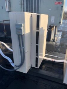 Two white HVAC units are installed on a rooftop, with electrical conduit and piping connected, and an RTU labeled "RTU-2" visible in the background.