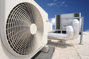 Close-up view of industrial HVAC units and ductwork mounted on a flat rooftop under a blue sky.