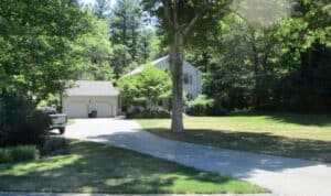 Two-story house with attached two-car garage, surrounded by trees and a large lawn, with a curved driveway leading to the garage.