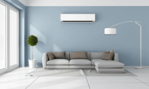 Modern living room with a light gray sectional sofa, floor lamp, potted plant, and wall-mounted air conditioner against a blue accent wall.