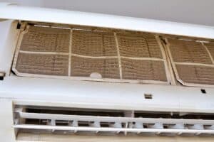 Close-up of an air conditioner with visible dust and dirt buildup on the filter and interior surfaces.