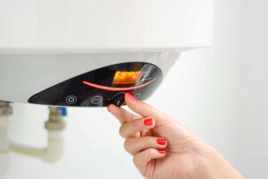A hand with red nail polish adjusts the temperature setting on a digital water heater control panel.