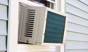 A window-mounted air conditioning unit installed in a residential window, with siding visible on the exterior wall.