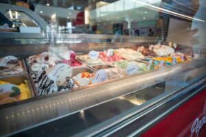 Display case with various flavors of gelato, each labeled with a small sign, inside a brightly lit ice cream shop.
