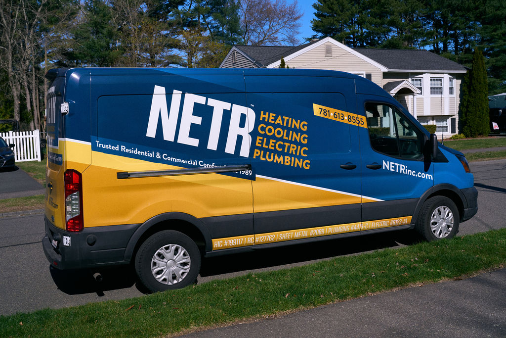 A NETR Inc. service van is parked on a residential street, featuring company branding and contact information for heating, cooling, electric, and plumbing services.
